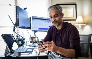 Interactive Brokers Stock Surges 16.4% Last Month A man trading stocks on his phone at his desk with a lot of computers around him.